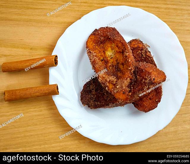 Traditional homemade Spanish Torrijas in a white dish decorated with two cinnamon sticks. Top View