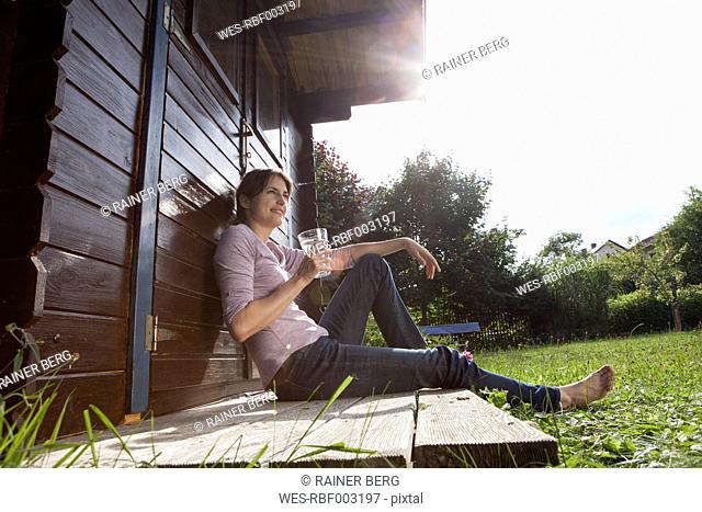 Smiling woman sitting at garden shed with glass of water