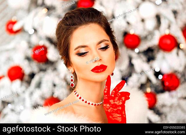 Winter portrait of Elegant woman with ruby jewelry set and red gloves. Beautiful brunette lady with wedding hairstyle, beauty makeup wears posing over xmas tree...