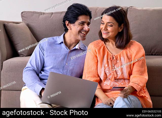 Happy Indian middle age couple shopping online through laptop using credit card