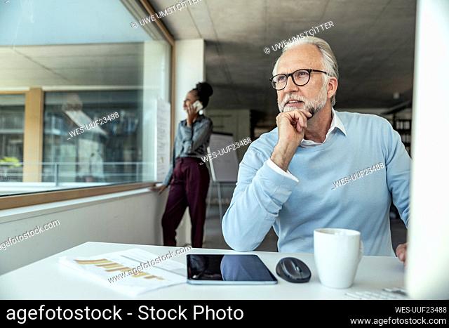 Thoughtful businessman with hand on chin while female colleague talking in background