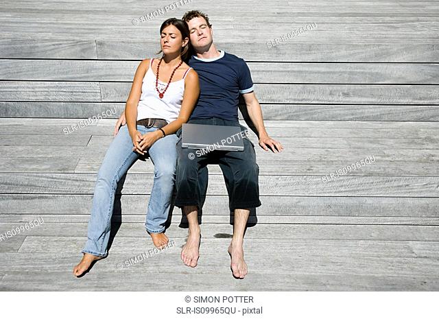 Couple lying on decking with laptop
