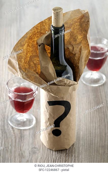 A bottle of red wine in a paper bag with a question mark
