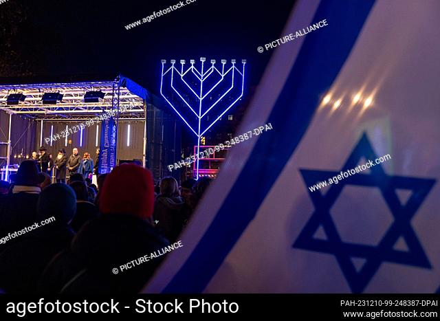 10 December 2023, Hesse, Frankfurt/Main: An Israeli flag is seen in front of a Hanukkah candelabra during the public lighting of the Hanukkah festival in...