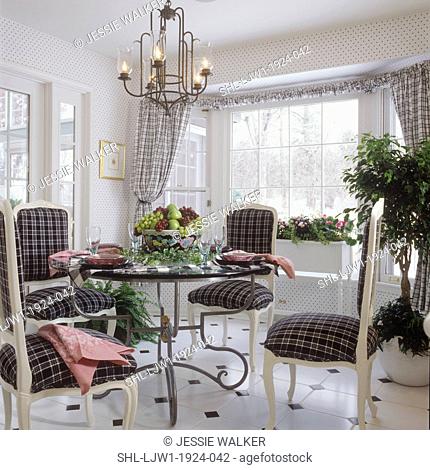 DINING ROOM: Round glass table with scroll iron base, French style side chairs, painted white wood, upholstered in black and white plaid, bowl of fruit