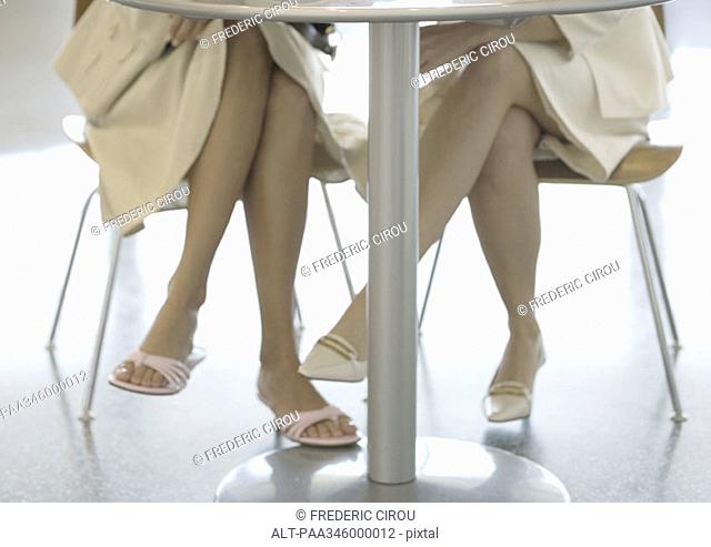 Two women sitting at table, view of legs under table