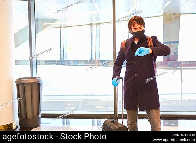 Reisender mit Mundschutz schaut auf die Uhr im Flughafen bei Covid-19 Pandemie