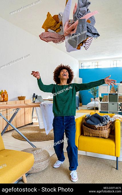 Happy young woman throwing clothes in living room at home