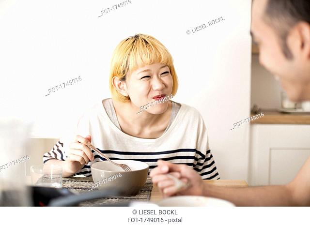 Happy young woman making face while having breakfast with man in house