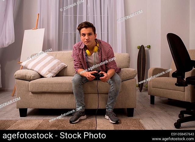 Teenage boy sitting on sofa playing computer games. Young boy at home, concerned with computer games