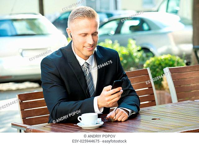 Businessman Sitting On Bench Listening Music On Cellphone