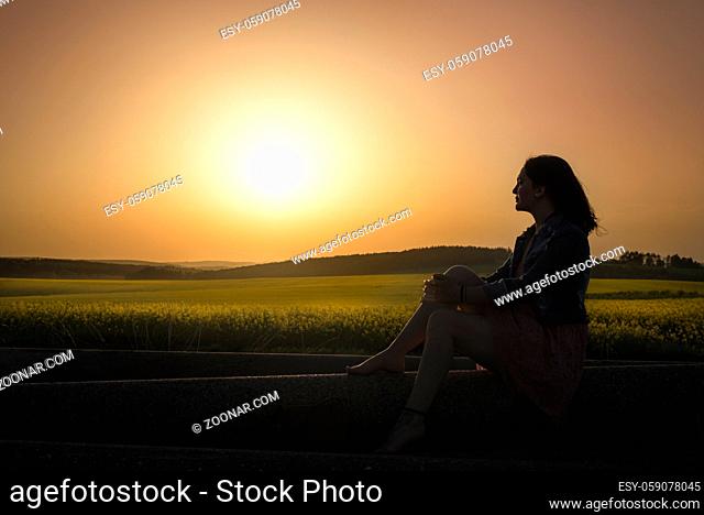 Silhouette of a woman gazing the horizon, admiring the sunset over rapeseed fields, in South Moravia, Czech Republic