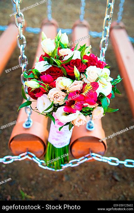 Wedding decoration of a beautiful delicate bouquet lying down on a swing in the park against green background