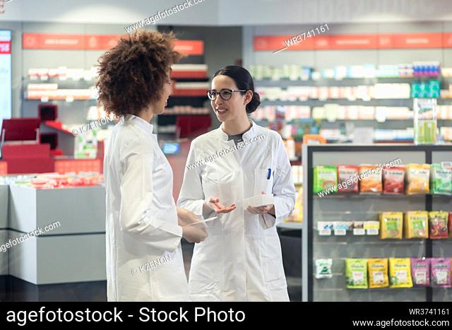 Two friendly female colleagues talking about medicines and prescriptions while working together as pharmacists in a modern drugstore