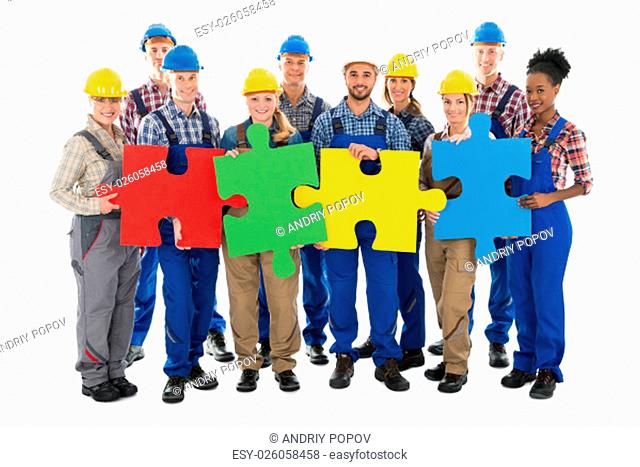 Portrait of confident construction workers joining jigsaw pieces against white background