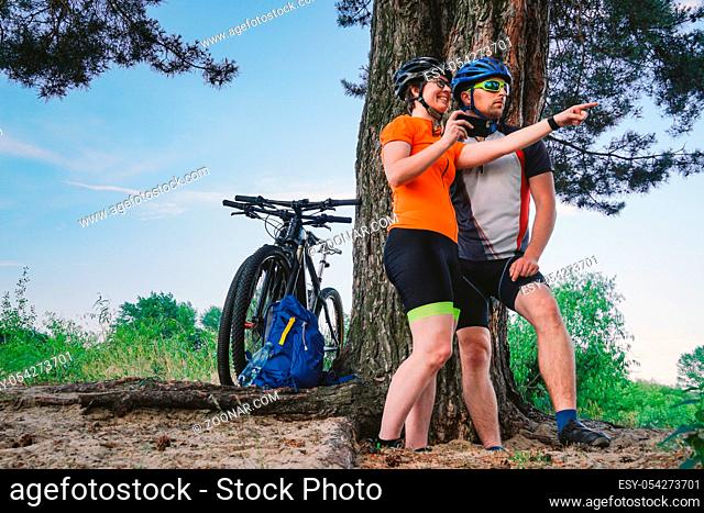Happy couple searching on map in smartphone destination. man and woman in helmets traveling mountain biking over rough terrain