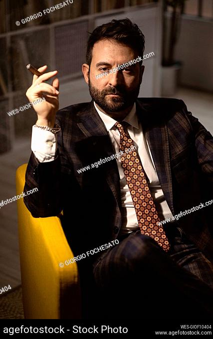 Portrait of bearded man sitting in armchair with cigar in hand