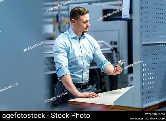 Male professional examining machine part on table in factory