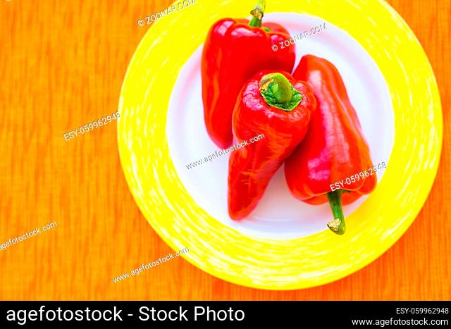 three red peppers on a colorful plate closeup