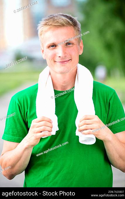Tired man with white towel after fitness time and exercising in city street park at beautiful summer day. Sporty model caucasian ethnicity training outdoor