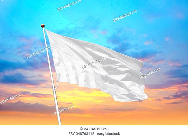 Blank white flag on pole waving in the wind in the background of cloudy sky at sunset. Colorful outdoor picture with empty flag mockup