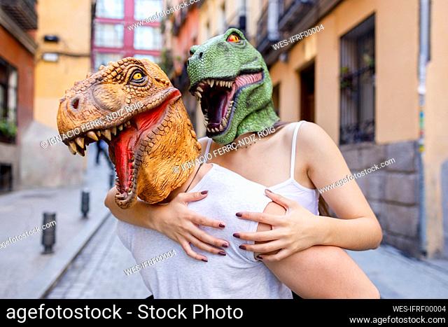 Male giving piggyback ride to female in dinosaur mask in city