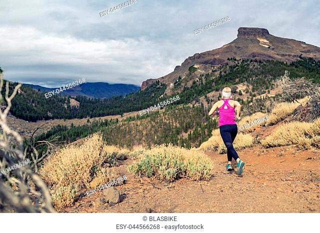 Trail running girl in mountains on rocky path. Cross country runner training in inspiring nature, dirt footpath on Tenerife, Canary Islands Spain