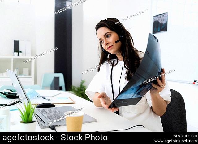 Female doctor showing x-ray image while consulting online through laptop at clinic