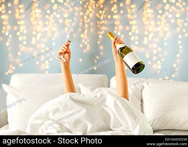 hands of woman lying in bed with champagne