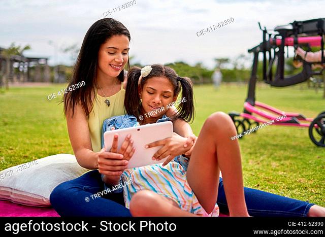 Mother and disabled daughter using digital tablet on blanket in park