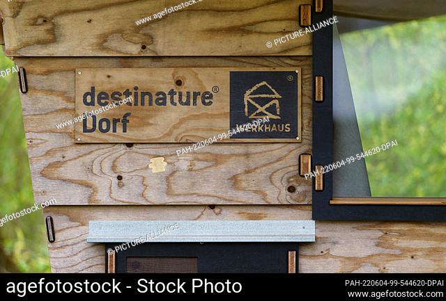 PRODUCTION - 03 May 2022, Lower Saxony, Hitzacker: ""Destinature village"" is written on a wooden sign. Mini wooden cabins invite visitors to spend the night