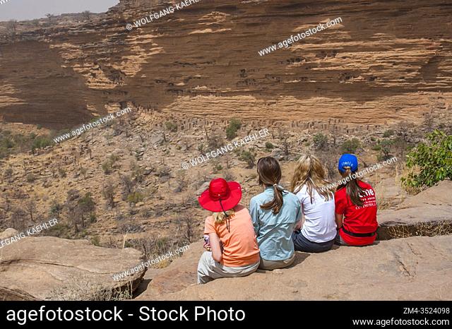 Tourists looking at a Dogon village and the Cliffside dwellings of the former Tellem tribe (13th century) in the Bandiagara Escarpment in the Dogon country in...