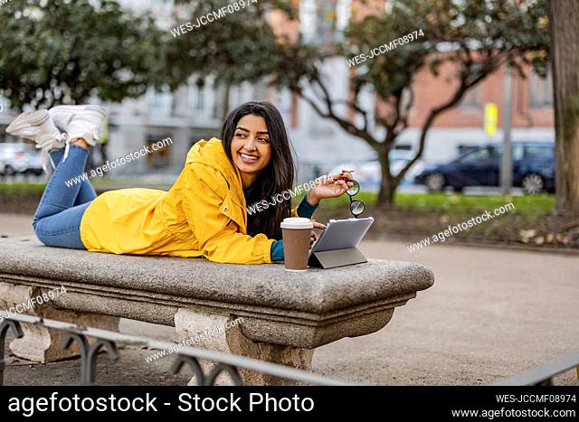 Thoughtful woman lying with tablet PC and disposable cup on seat