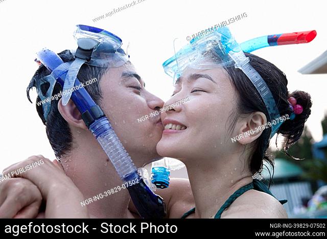 Smiling couple kissing on the cheek wearing snorkeling gear in the pool