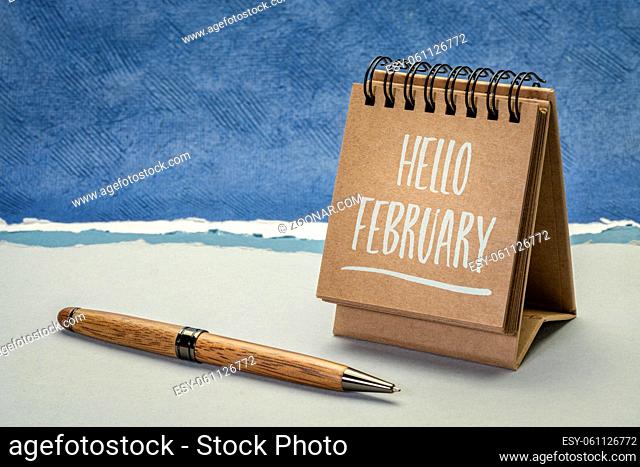 hello february greeting card - handwriting in a spiral desktop calendar against abstract paper landscape, calendar concept