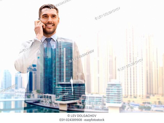 business, technology, communication and people concept - young smiling businessman calling on smartphone over dubai city background with double exposure effect