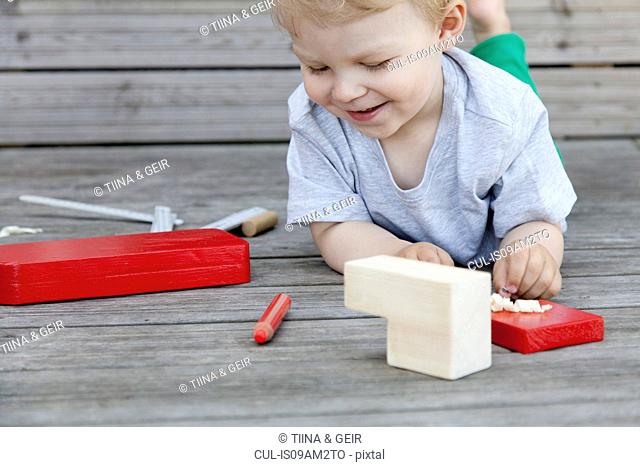 Male toddler playing with wooden blocks for toy boat on pier