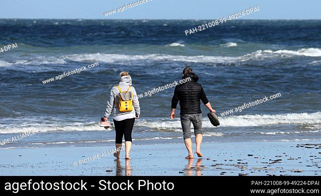 PRODUCTION - 06 October 2022, Mecklenburg-Western Pomerania, Warnemünde: A man and a woman are barefoot on the Baltic Sea beach