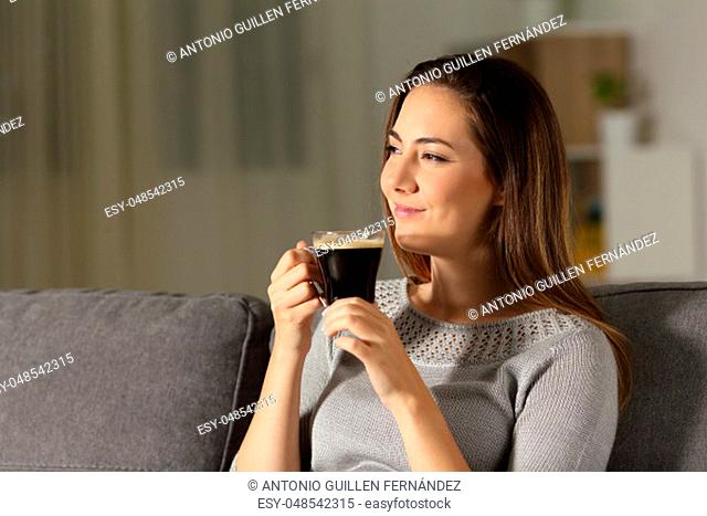 Satisfied woman enjoying coffee in the night sitting on a couch in the living room at home