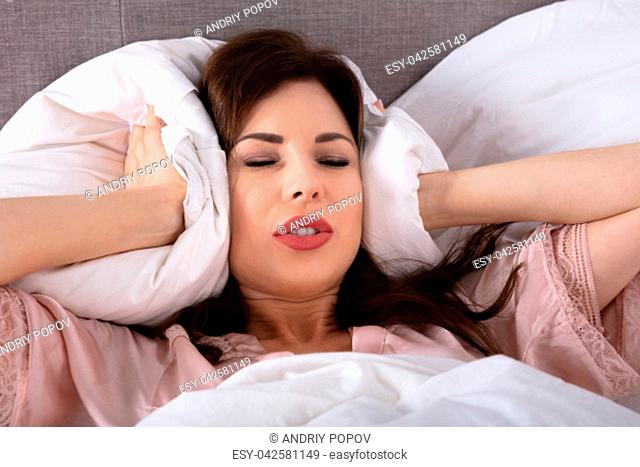 Disturbed Woman Covering His Ears With Pillow While Lying On Bed