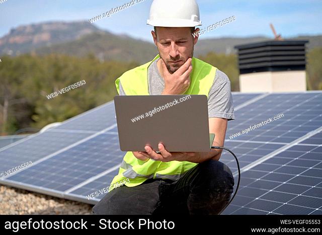 Engineer with hand on chin using laptop in front of solar panels