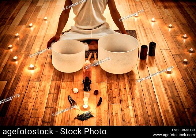 Man sitting in indian behind his two musical crystal bowls, with a display of sacred object and surrounded by candles