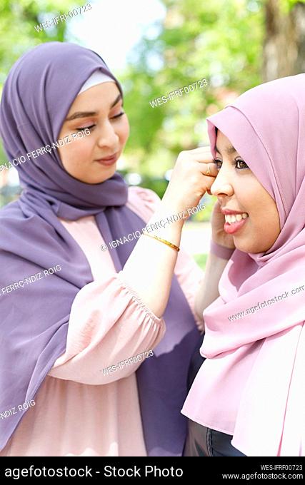 Woman adjusting hijab of female friend in public park