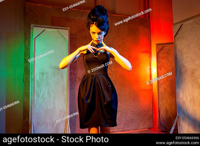 Young female model with hair style in black dress posing on background of grunge decorations