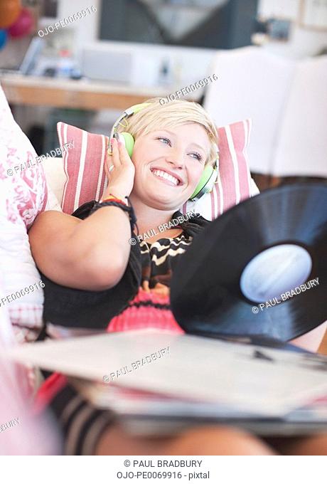 Woman laying on sofa listening to headphones and holding music record