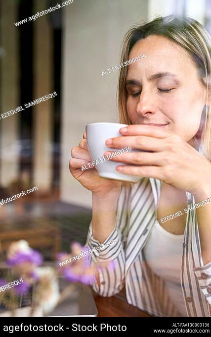 Portrait of attractive woman holding cup of coffee in her hands with eyes closed
