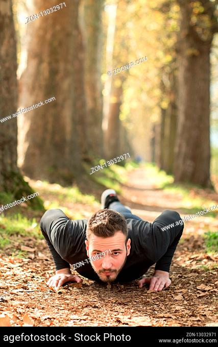Photo of handsome nice guy outdoors at morning. Young man doing push up exercises while training in park