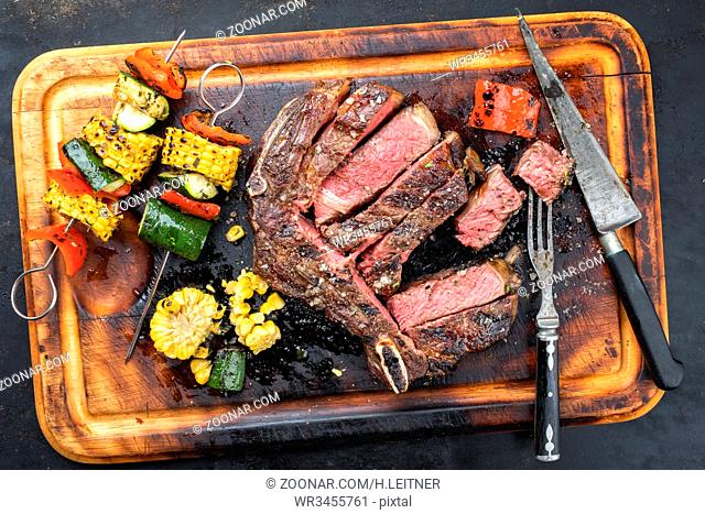 Barbecue dry aged wagyu cutlet with vegetable skewer as top view on a burnt cutting board
