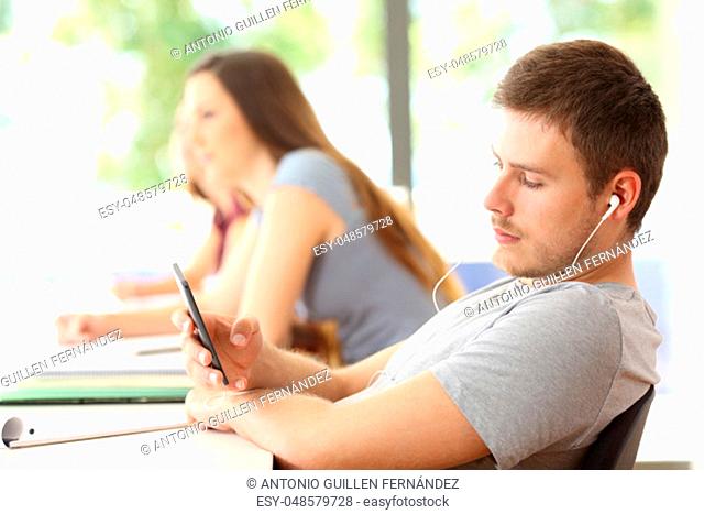 Bad student distracted listening to music sitting in a classroom