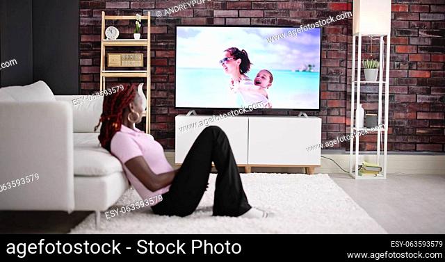 Young Woman Sitting On Carpet Watching Movie On Television At Home